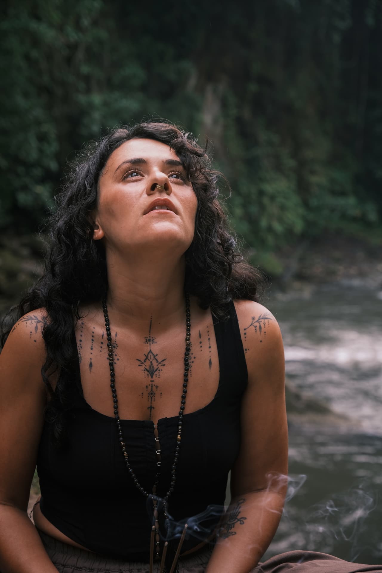 Nicole seated by water in the forest, looking upward